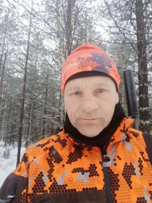 Heikki Moilanen oranssit metsästysvaatteet päällä ja kivääri selässä