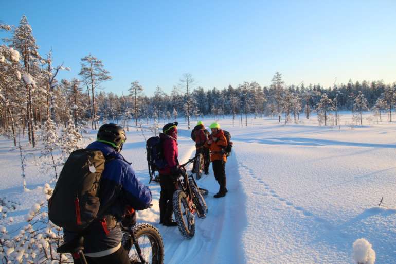 Neljä ihmistä läskipyöräilee lumisen maiseman keskellä